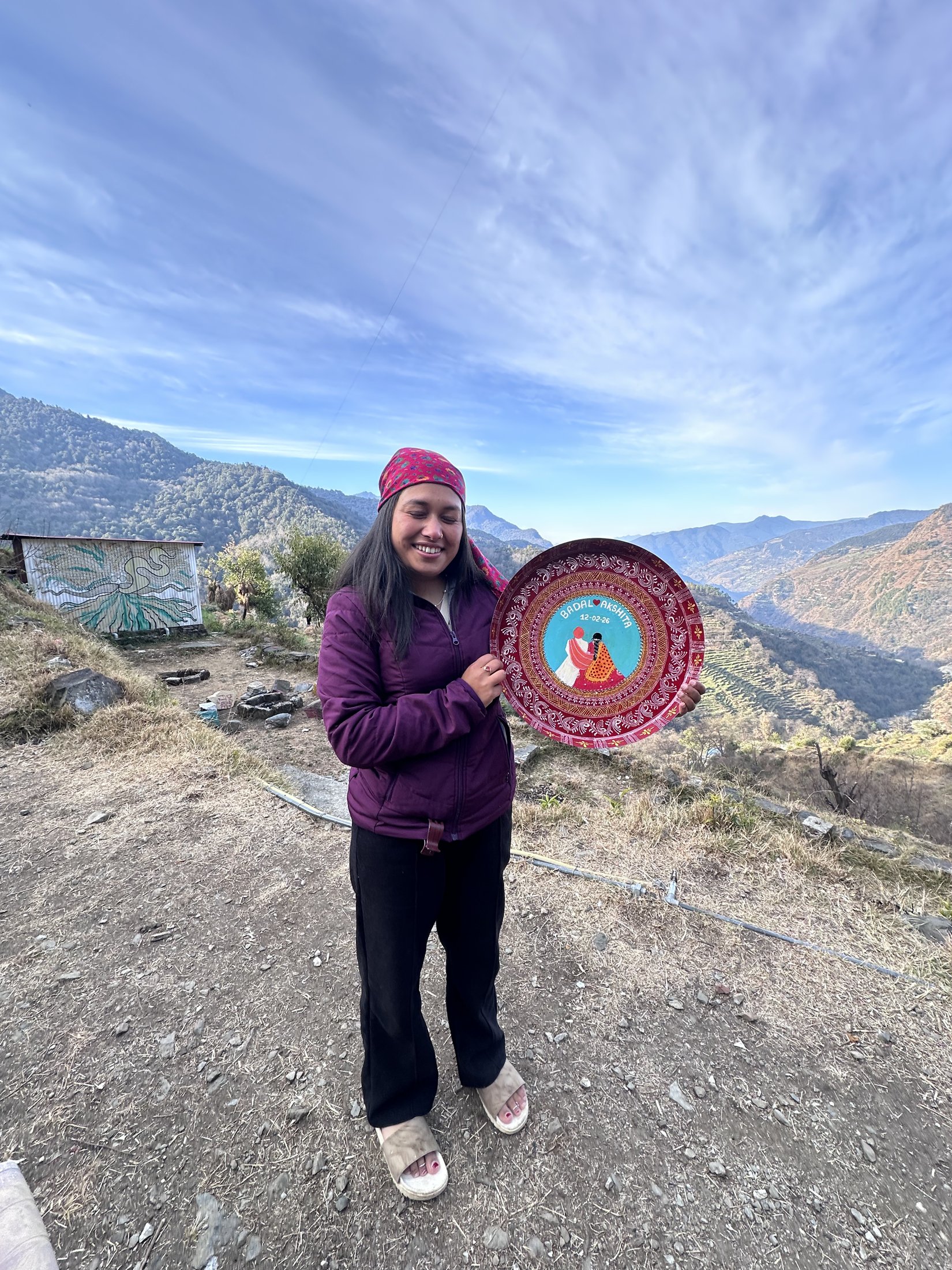Kajal holding a finished Aipan plate with the Himalayan valley behind her