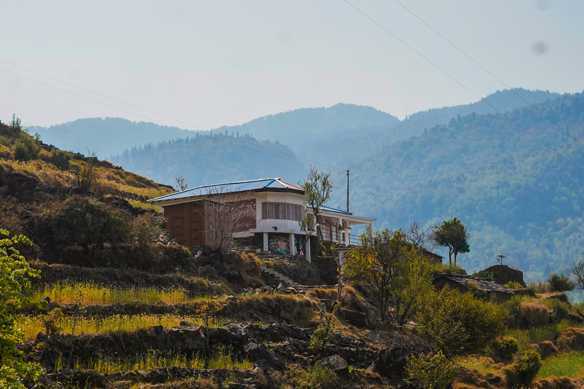 The Aipan Retreat — a small mountain home nestled into terraced hillsides with forested Himalayan ridges behind it